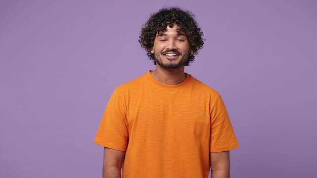 Smiling cheerful fun cool satisfied happy young Indian man he wearing orange t-shirt casual clothes looking camera isolated on plain pastel light purple background studio portrait. Lifestyle concept