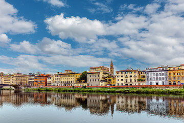 The Arno River Embankment reveals charming architecture in Florence, Italy. Colorful buildings line the water, reflecting the vibrant skyline under a blue sky.
