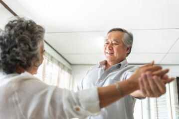 Fototapeta premium Asian Senior couple Celebrating Wedding Anniversary. Elderly man and woman dance joyfully in their living room. share smiles and laughs, enjoying each other.