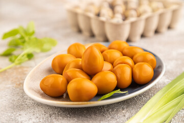 Pile of smoked quail eggs on plate on a brown concrete background. side view, close up, selective focus.
