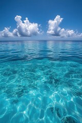 Obraz premium Serene ocean vista with turquoise water reflecting sunlight under a clear blue sky adorned with fluffy white clouds offering a tranquil summer escape