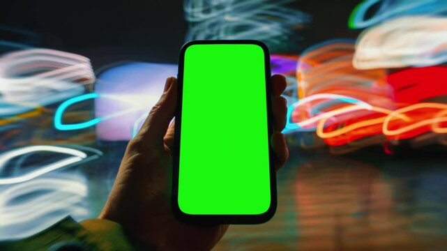 Close-up time-lapse hyperlapse of male hand holding modern smartphone keylight green screen gadget walking city street at night, fast motion blurry light trails glow, pov cellphone, chroma key