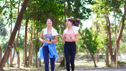 Two young Asian women jogging together in a green park, enjoying outdoor exercise and a healthy...