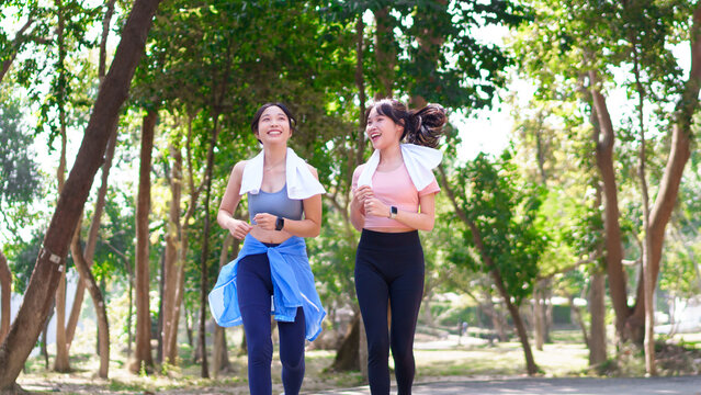 Two young Asian women jogging together in a green park, enjoying outdoor exercise and a healthy lifestyle