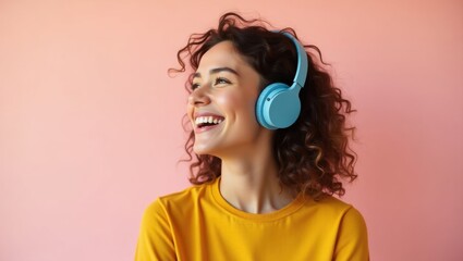 Fototapeta premium Happy Young Woman with Curly Hair Listening to Music on Blue Headphones Against Pink Background