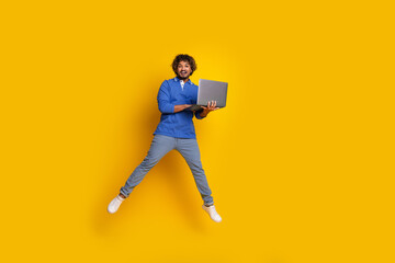 Energetic Young Man Jumping with Laptop Against Bright Yellow Background, Exuding Joyful Expression
