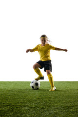 Naklejka premium Concentrated girl in yellow jersey and black short, soccer player training on grassy surface, dribbling ball against studio background. Concept of sport, childhood, game, competition, activity