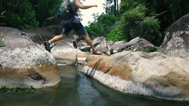 A tourist walks from stone to stone in a riverbed in the jungle