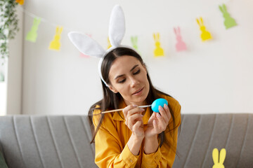 Woman painting easter eggs wearing bunny ears headband