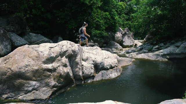A tourist walks on huge rocks along a mountain river in the jungle