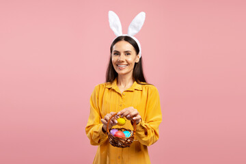 Smiling woman wearing bunny ears holding easter eggs basket