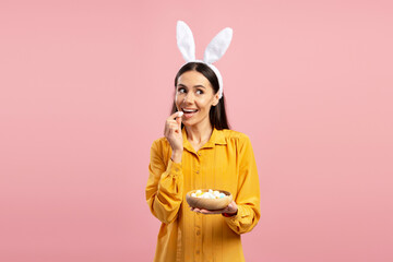 Happy woman wearing bunny ears headband eating colorful easter eggs candies