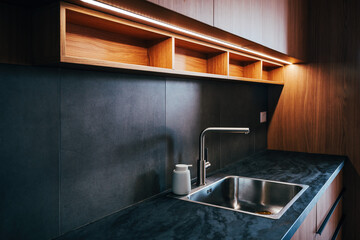 Water faucet and metallic sink in modern sleek kitchen with led strip light