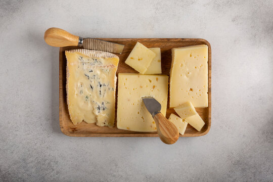 Cheese plate on concrete background. Italian cheeses - caciotta with fenugreek, blue cheese and asiago on wooden board. Cheese platter. Top view. Copy space.