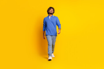 Fototapeta premium Happy young man in casual blue outfit walking confidently against a vibrant yellow background, displaying leisure and lifestyle