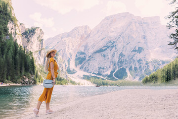 Naklejka premium woman enjoys fresh air at Lago di Braies. girl in yellow dress and boater.