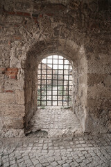 Fototapeta premium Small grated doorway in the thick brick wall surrounding Kalemegdan Tower Castle. Belgrade, Serbia. Close-up of rusted iron portcullis corroded bars framed by cracked stone arch