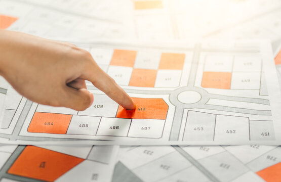 Hand pointing to cadastral map to decide to buy land. real estate concept with vacant land for building construction and housing subdivision for sale, rent, buy, investment.