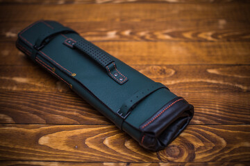 Elegant Green Leather Roll-up Bag with Stitch Details on Wooden Table Surface