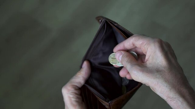 Hands of an elderly man with the last coin in an empty wallet