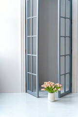 Interior on a white background with an open window and a vase with tulips on the floor