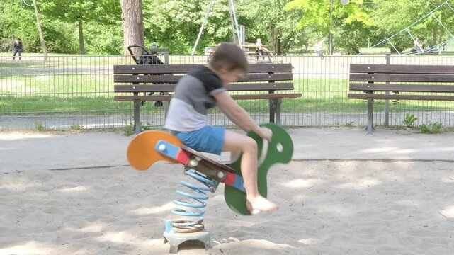 joyful child bounces excitedly on spring horse at playground, Childhood joy, Playful moment, summer entertainment, training in coordination movements, stimulation vestibular apparatus