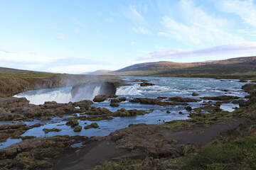 A breathtaking view of the Godafoss waterfall in northern iceland, surrounded by rugged terrain and a wide glacial river
