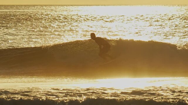Young male surfer catches a wave in the ocean and rides on it during sunset time. Side view video