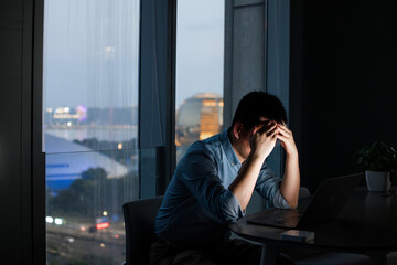 tired asian man overtime in office with laptop