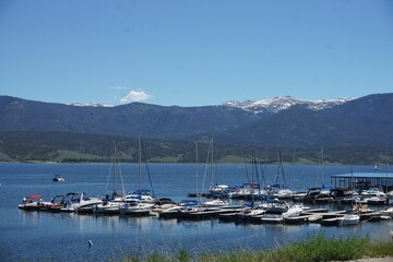View of a marina with boats on a clear lake against a backdrop of mountain ranges
