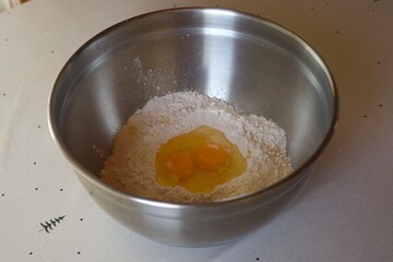 Flour and cracked eggs in a metal bowl
