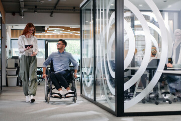 Business colleagues, collaborative business colleagues, including a person in a wheelchair, walk...