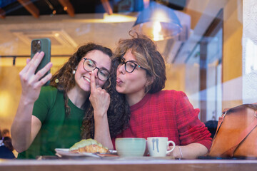 Two playful women taking a selfie while having breakfast at the coffee shop