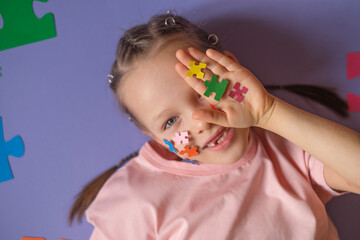 A pretty girl shows a palm with pieces of multicolored paper jigsaw puzzles as a sign of support for Kids with autism spectrum disorder. Education and child development