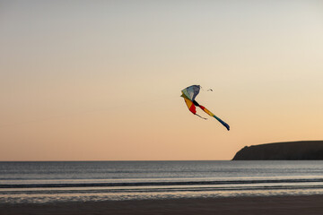 Evening at the beach with a boy flying a kite. Silhouette against sunset over the sea, evoking freedom, play, and peaceful coastal atmosphere.