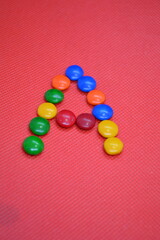 colored chocolate coated candy alphabet on pink background A
