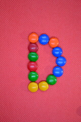 colored chocolate coated candy alphabet on pink background D