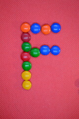 colored chocolate coated candy alphabet on pink background F