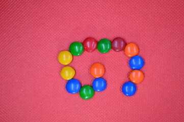 colored chocolate coated candy alphabet on pink background G