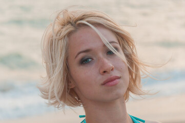 Portrait of a Blonde girl in a turquoise dress standing on the seashore at sunset