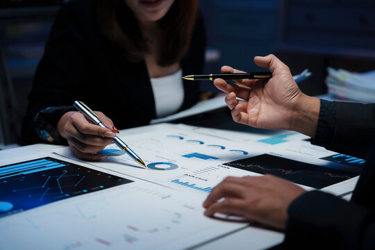 Professional team analyzing financial reports, pointing at charts while discussing market performance in collaborative office meeting, tracking business metrics and strategic insights - Powered by Adobe