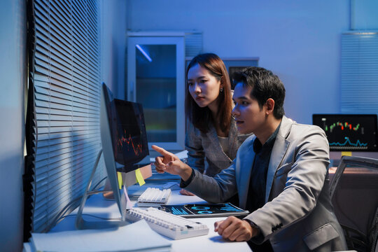 Financial analysts examining cryptocurrency charts late at night, collaborating closely while pointing at computer screen and evaluating digital investment risks