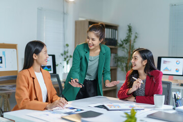 Smiling Asian businesswomen discussing and brainstorming together during a meeting, analyzing financial charts and graphs showing company growth and success