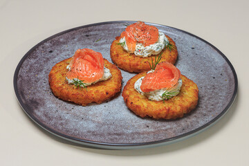 plate with three savory potato pancake or fritter-style dishes, each topped with a creamy white spread and a slice of smoked salmon. 