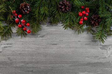 Christmas decorative upper border with green spruce, cones and holly berries on old wooden...
