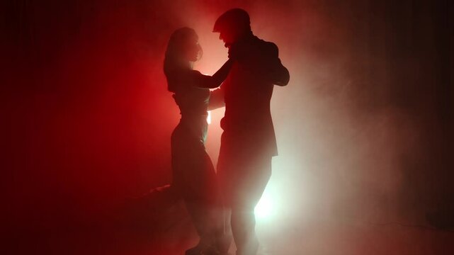 A tango dance instructor and student perform a passionate and elegant routine in the mist. Dramatic lighting enhances the aesthetic and emotional intensity of the dance.