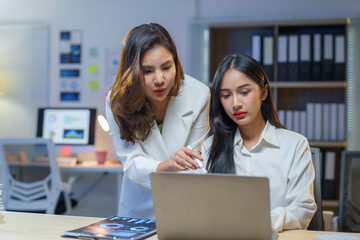 Fototapeta premium Professional Asian women collaborating late at night, reviewing financial charts on laptop and strategizing corporate development with focused teamwork