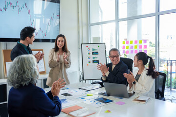 Asian business team clapping enthusiastically during meeting, celebrating collaborative achievement, professional workspace with data visualizations surrounding colleagues