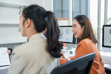 Obraz premium Group of young Asian businesswomen discussing marketing strategy using charts on computer and clipboard in office, smiling and working together on new project