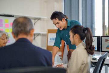 Diverse asian business team collaborating, reviewing financial charts and strategizing corporate growth in contemporary workspace